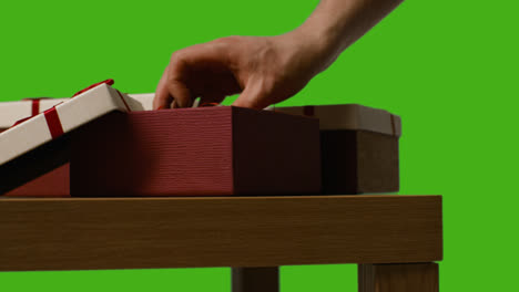 Close-Up-Of-Man-Putting-Present-Into-Gift-Wrapped-Box-On-Table-Shot-Against-Green-Screen-1